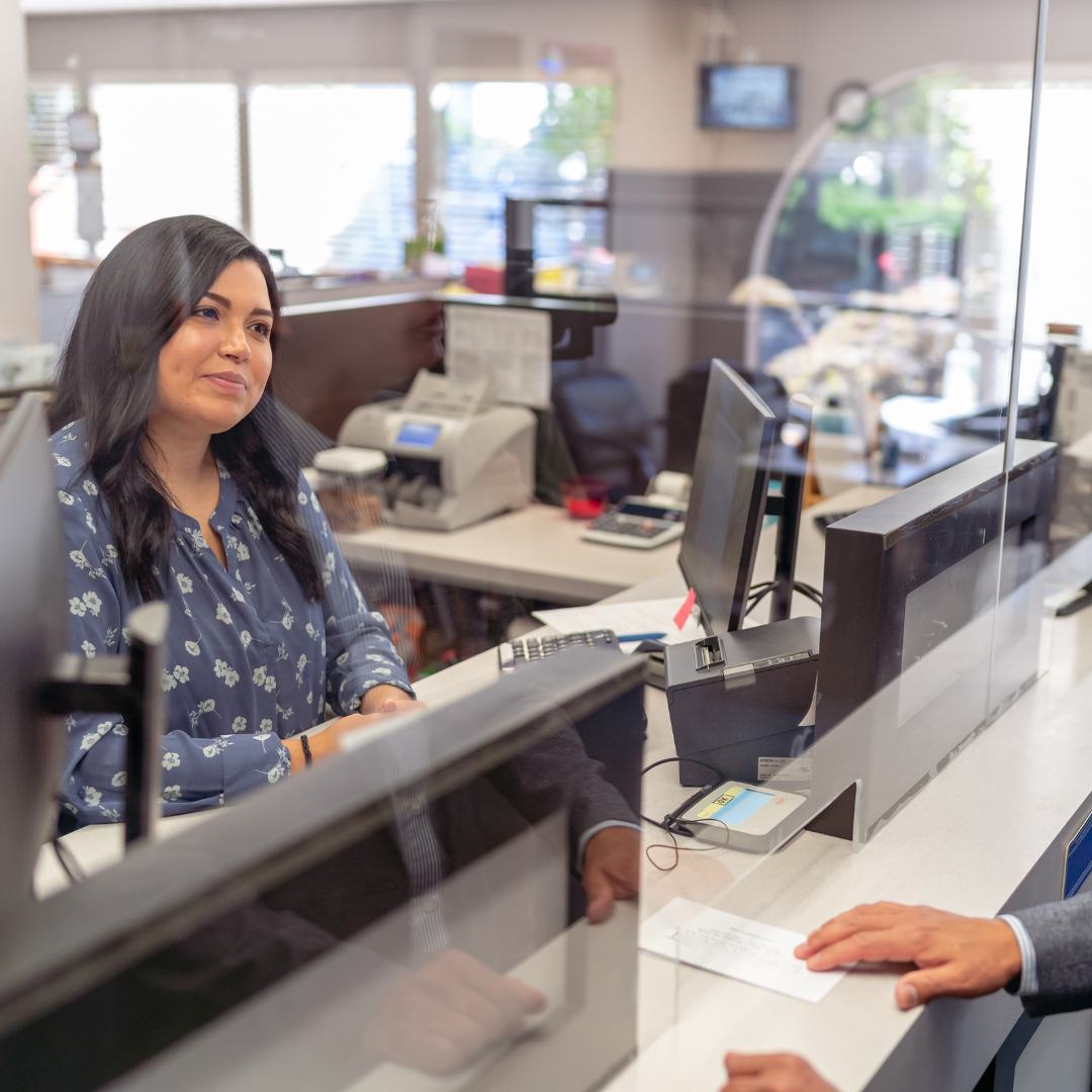 bank teller helping behind glass wall helping customer 