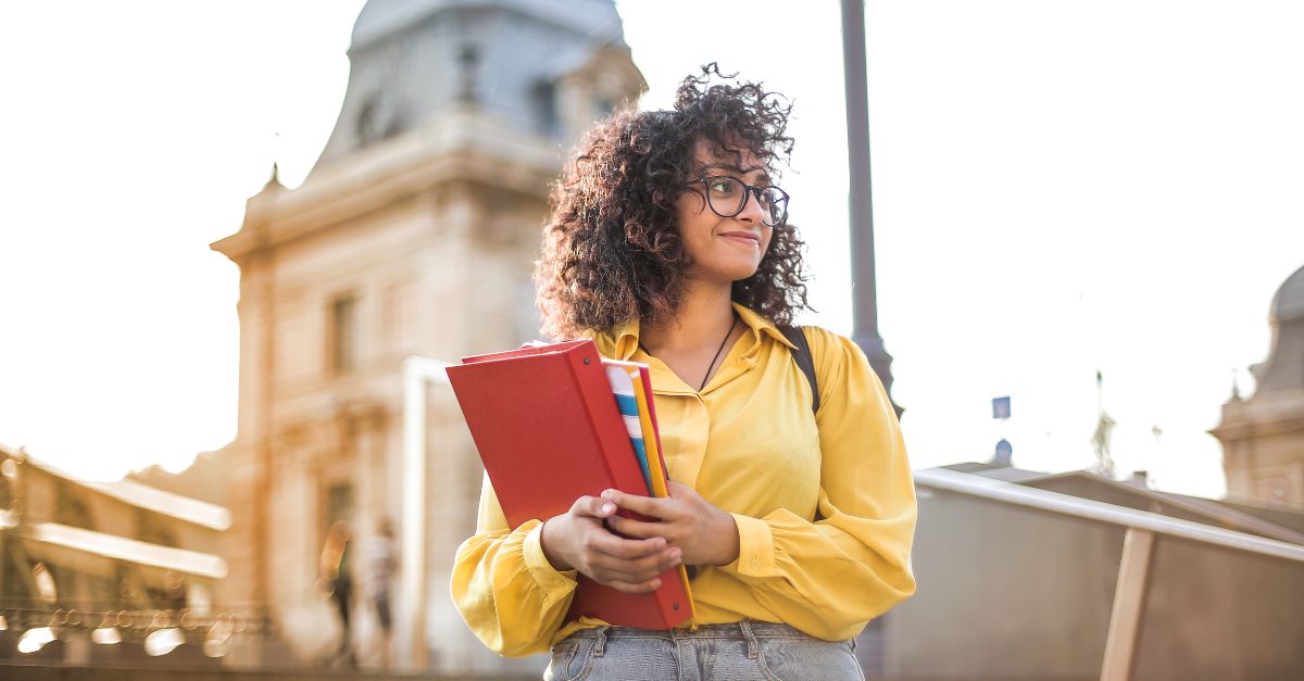 طالبة تحمل كتباً أمام مبنى الكلية 